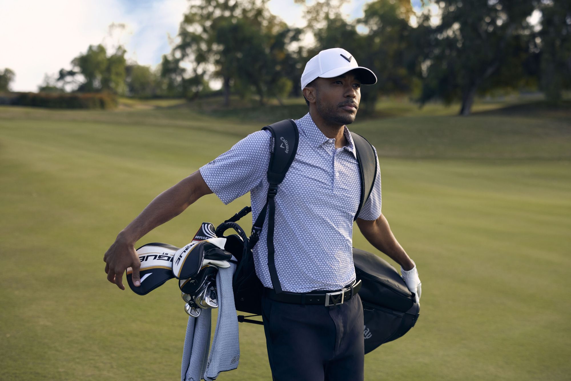 Male golfer on a fairway wearing a cap, polo, golf trousers and a golf bag