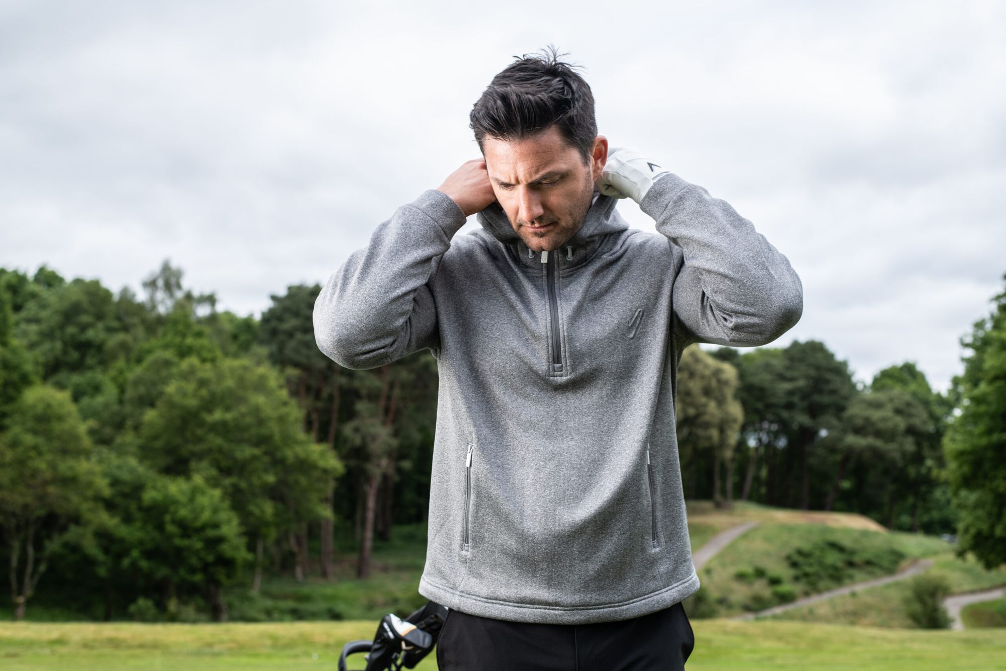 Male golfer on a golf course adjusting the collar on his sweater.