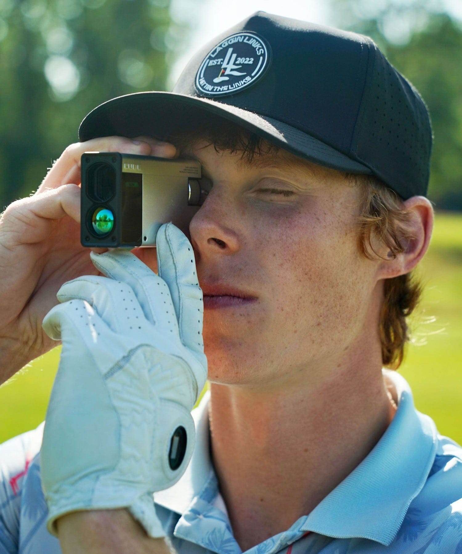 A golfer holding the CUBE Rangefinder to his eye on a golf course.