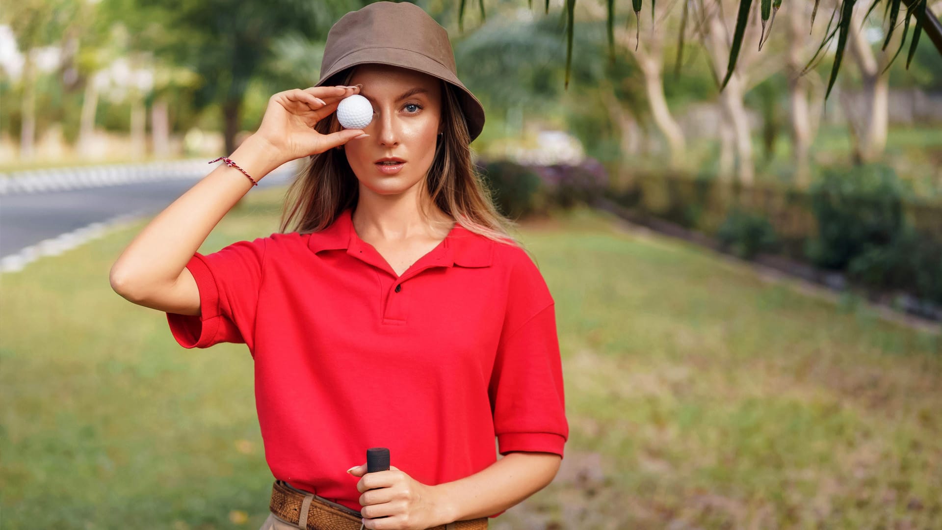 A woman golfer holding a golf ball in front of her eye