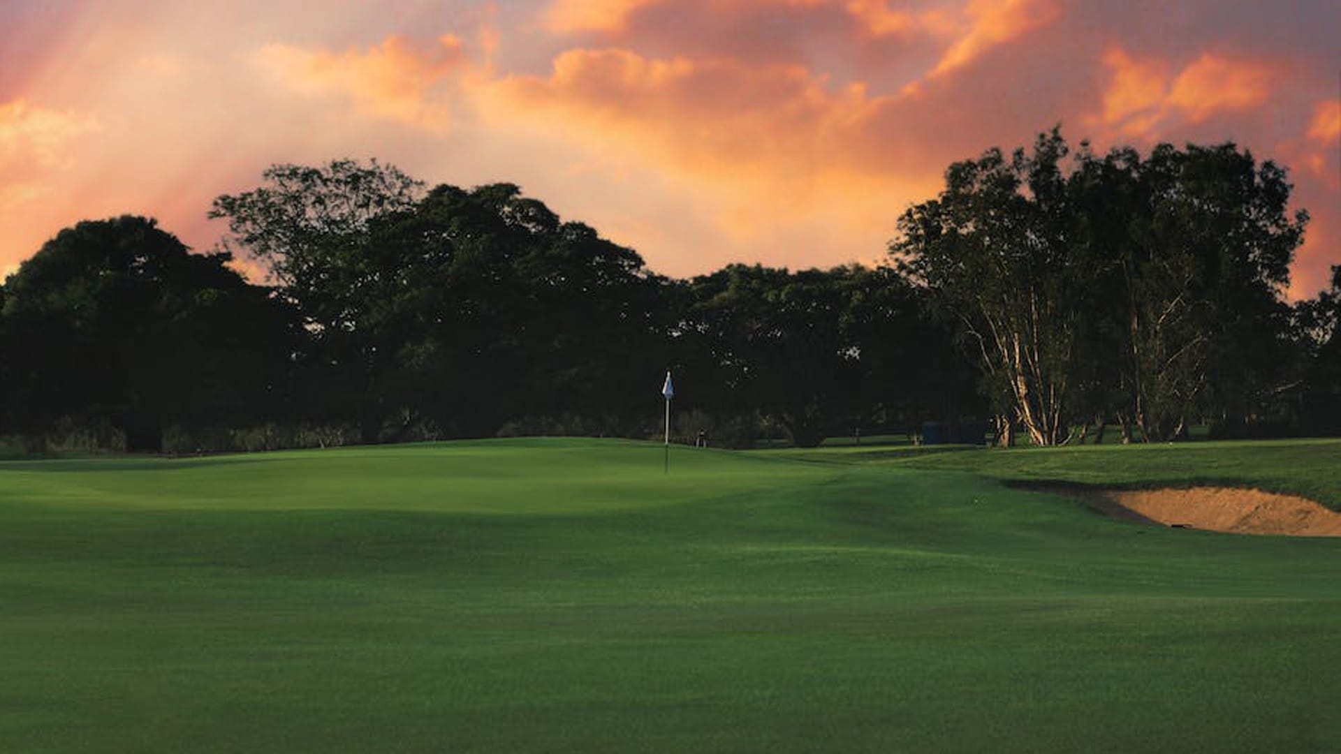 A photo of a golf hole with a fiery sunset behind
