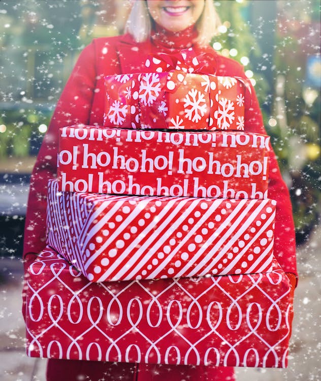 A smiling woman dressed in red carrying a stack of red presents
