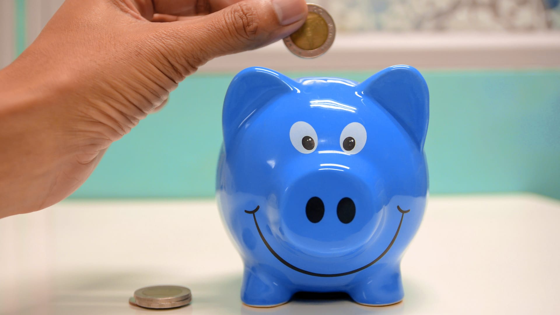 A blue piggy bank with a hand inserting coins