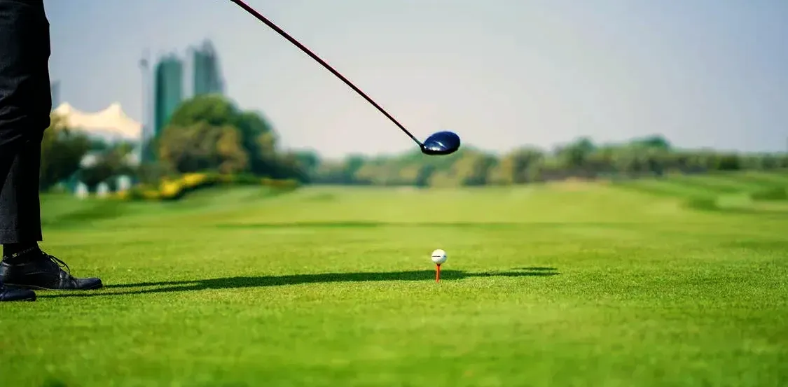 A golf ball on a tee ready to be struck by a golfer to the left