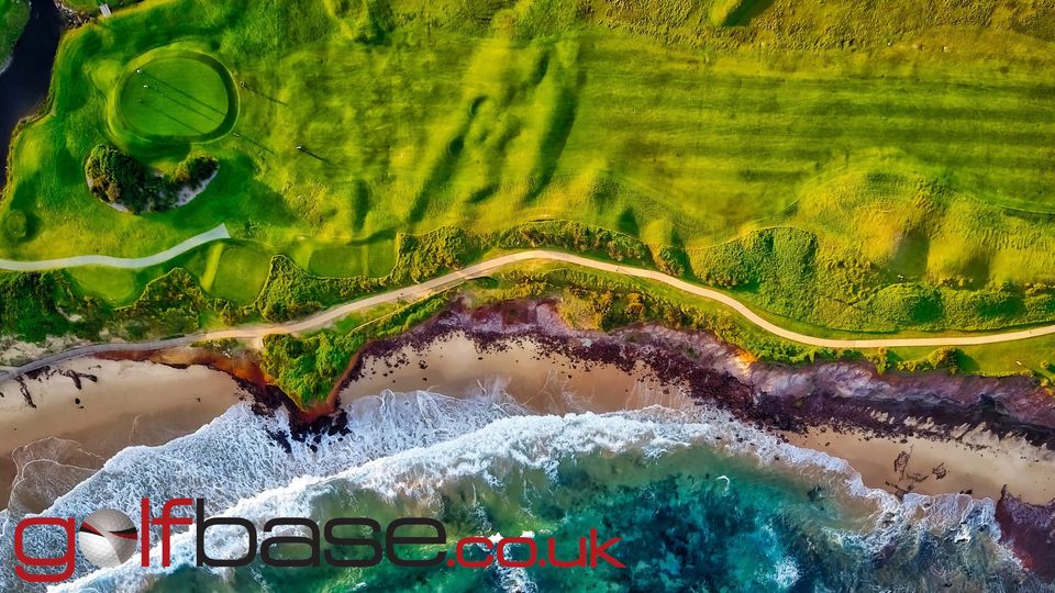 Aerial shot of a lush golf fairway and green next to the sea