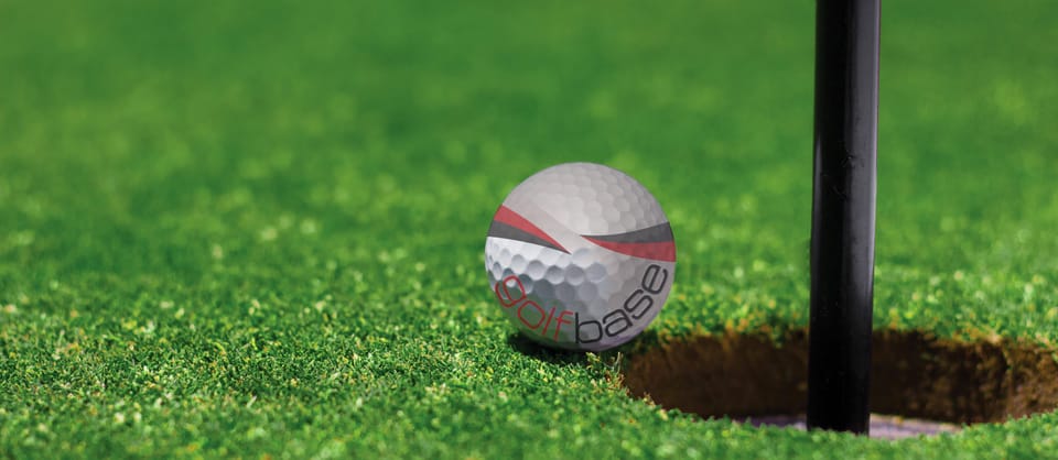 Photo of a golf ball bearing the Golfbase logo next to a hole